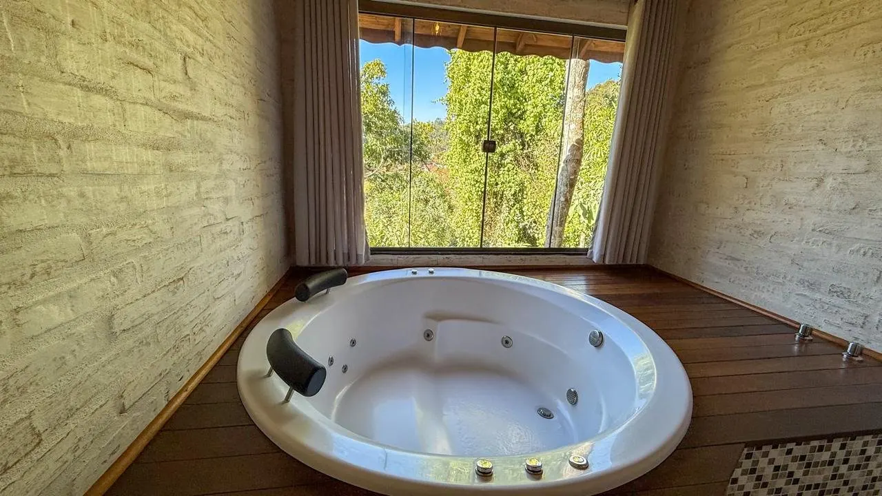 Hidromassagem redonda ao lado de uma janela com vista para a mata