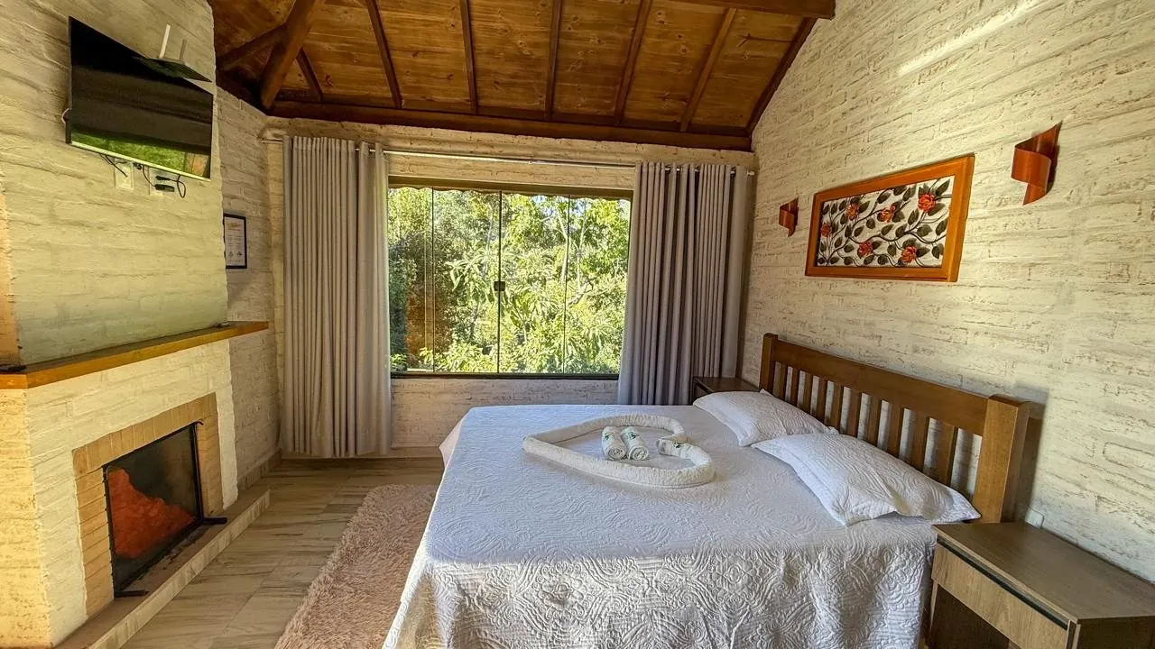 Quarto com lareira, cama de casal e janela para a mata