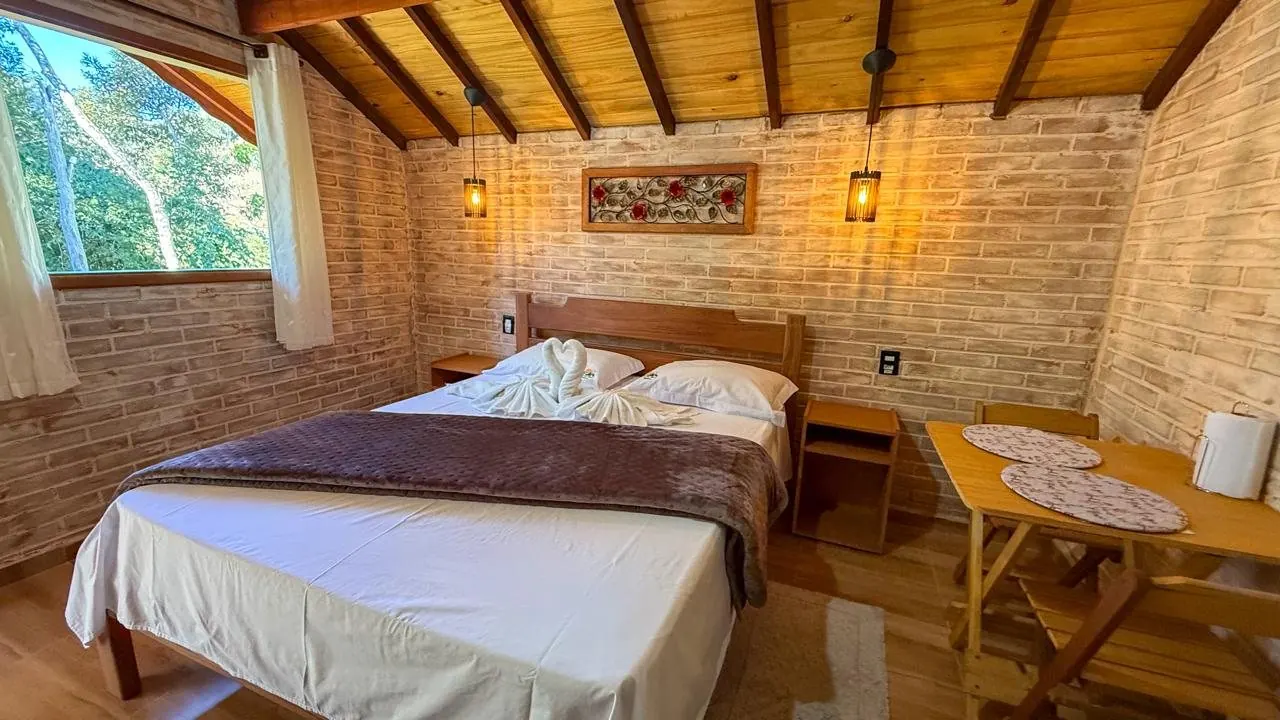 Quarto com cama queen, teto de madeira e parede de tijolinhos